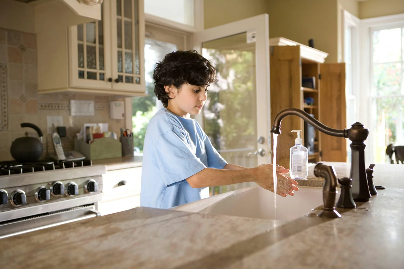 A boy washing his hands with clean water at the kitchen sink